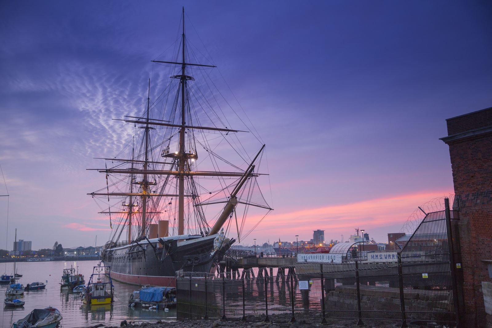 HMS Warrior at dusk, against a purple sky. Image provided by Portsmouth Historic Dockyard